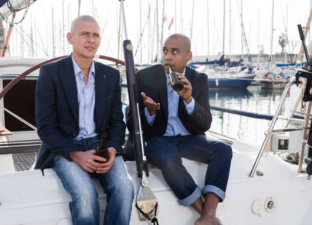 Latin American and European businessmen sit and drink beer on the yacht in seaport