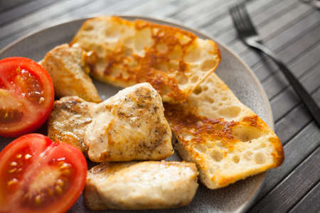 toasted pieces of chicken breast, toast and tomatoes on a breakfast plate