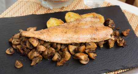 delicious fried trout fillet on pillow of fried champignon mushrooms on dark warm stone plateの写真素材