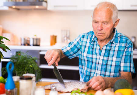 retired man preparing fish at home in the kitchenの写真素材