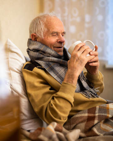 gray haired elderly man is sick and drinking hot tea at homeの写真素材