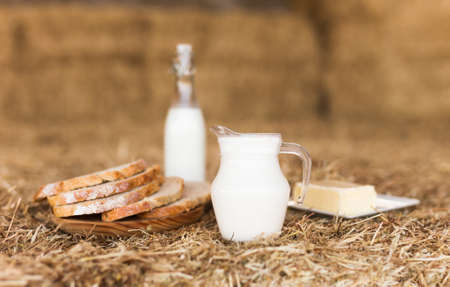 Milk bottle, slices of fresh wheat bread and butter on hayの写真素材