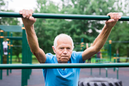 old cheerful pensioner man doing physical exercises on sports equipped playgroundの写真素材