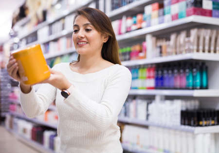 Portrait of happy hispanic girl shopping in cosmetics store, choosing hair care treatmentsの写真素材