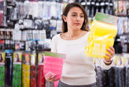 Young attractive long haired Latina choosing plastic hair rollers with velcro in cosmetics storeの写真素材