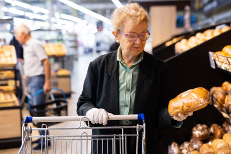 older european woman with glasses shopping in bread section of supermarketの写真素材