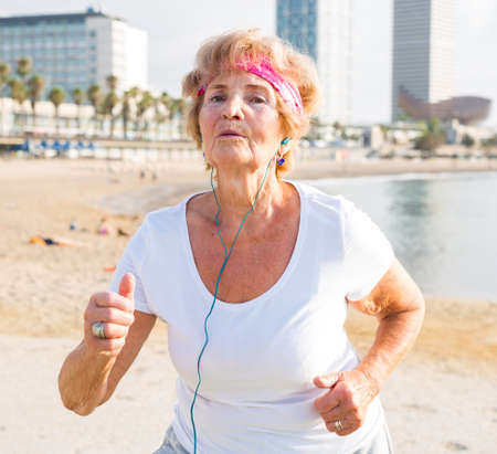 Pensioner in headphones jogging on the sea beachの写真素材