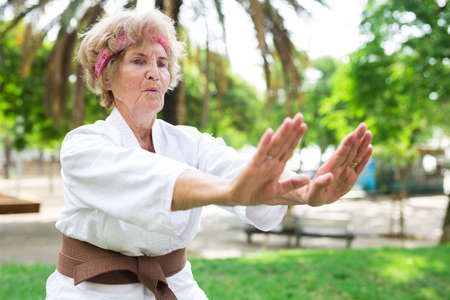Old lady in kimono performing karate moves in urban park.の写真素材