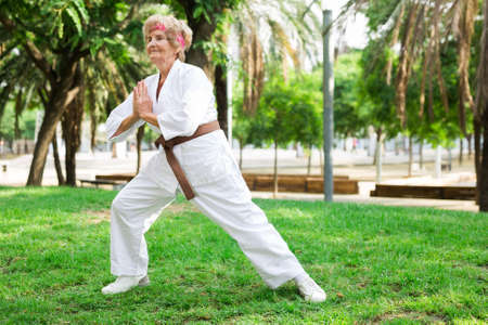 Mature woman in white kimono training in park. She's performing kata moves.の写真素材