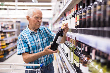 mature senor choosing alcoholic drinks in supermarketの写真素材