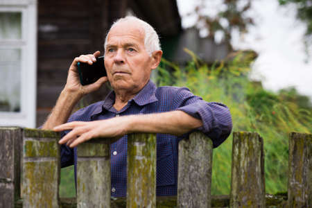 European senior man leaning on fence and talking on phone outdoors.の写真素材