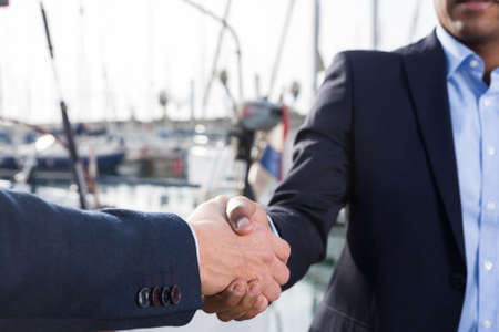 handshake of two businessmen near the yachts in the port