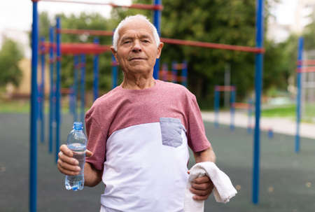 Mature man quenches her thirst from bottle after jogging in summer park