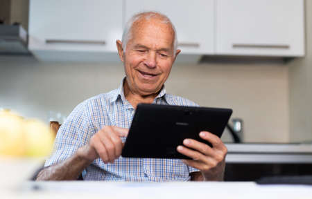 Modern elderly man using digital tablet to shop online from home