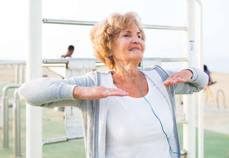 Mature woman in sportswear and headband doing fitness exercises outdoors.の写真素材