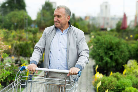 Middle aged caucasian man choosing seedlings and sprouts in garden center.の写真素材