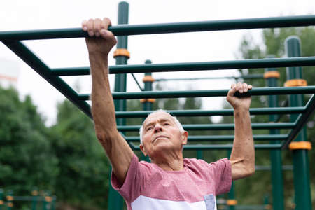 Old man climbing on horizontal ladder on outdoor sports ground.
