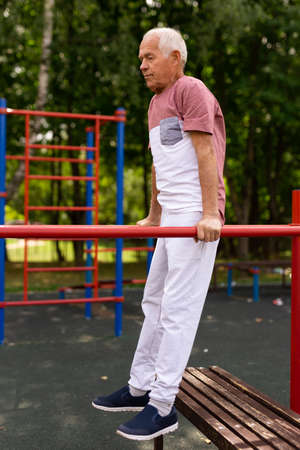 Senior man exercising at parallel bars in outdoor sports ground.