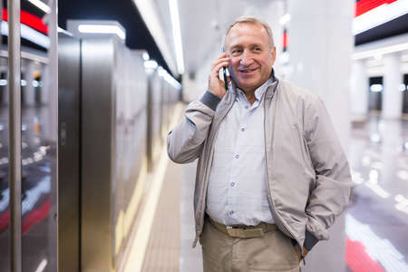 Middle aged man standing in subway station and talking on phone while waiting for train.