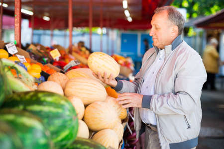 Middle aged european man buying fresh melons in fruit market.の写真素材