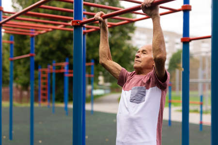 Active grandpa pulls up on horizontal bar on the sports ground