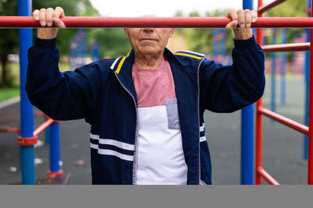 Active grandpa pulls up on horizontal bar on the sports groundの写真素材