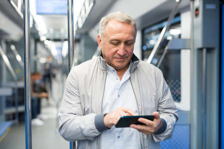 Mature man writing message on smartphone screen in subway trainの写真素材
