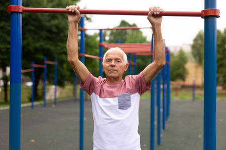 Active grandpa pulls up on horizontal bar on the sports groundの写真素材