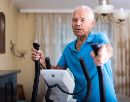 Senior man training on cross-trainer at home in living room.の写真素材