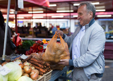European man standing in greengrocery beside counter and buying potatoes.の写真素材