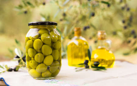canned olives in a glass jar, oil and olives on the table against the background of the olive gardenの写真素材