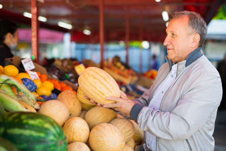 Man choosing melons in fruit shopの写真素材
