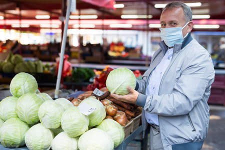 Man in mask buying cabbage in marketの写真素材