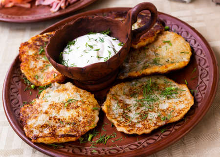 potato pancakes with sour cream and herbs on white plateの写真素材