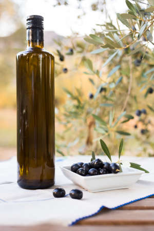 still life of olives and oil on a table against a background of olive treesの写真素材