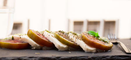 caprese salad with mozzarella, black tomatoes and pesto on black stone plate