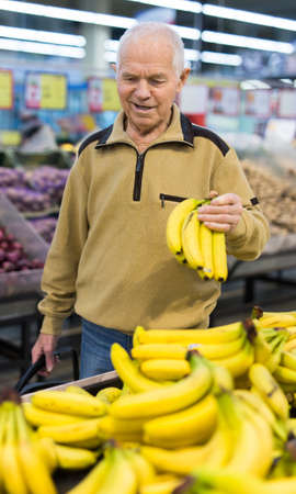 senor man pensioner buying banana in grocery in supermarketの写真素材