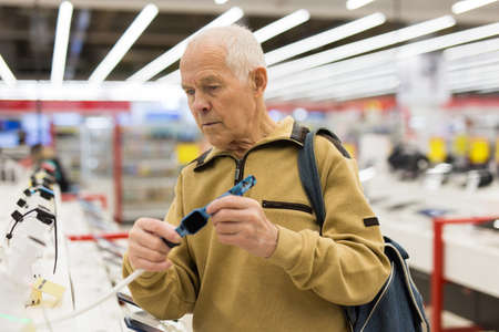 elderly man examines smart watch in showroom of electronics storeの写真素材