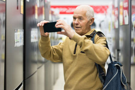 senor man pensioner scanning QR of fridge in showroom of electrical appliance store