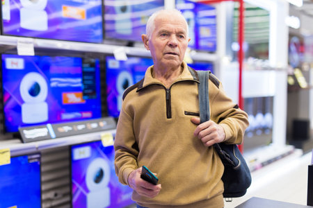senor man pensioner buying modern digital televisor with smart tv in showroom of digital electronic goods storeの写真素材