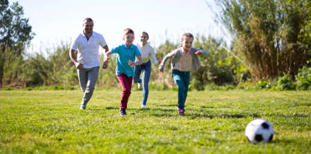 family with children playing soccer on the grass in the park