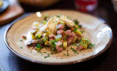 Delicious potato salad with slices of ham and mushrooms close up