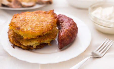 Fried grated potato pancakes with fried sausage on white plateの写真素材