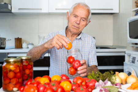old gray haired man makes harvests for the winter pickles tomatoesの写真素材