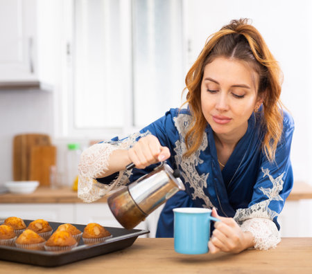 Upset just woken up woman in blue peignoir preparing coffee in kitchenの写真素材