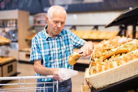 elderly man buying bread and pastries in grocery section of the supermarketの写真素材
