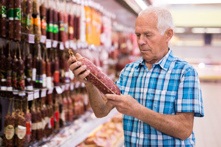 mature senor choosing uncooked smoked sausages in sausage department supermarketの写真素材