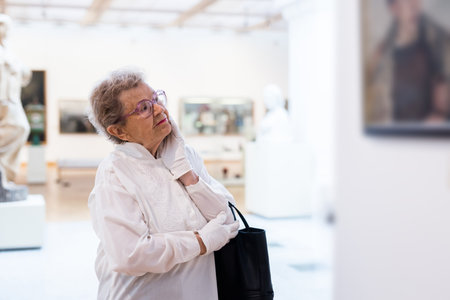 mature woman examines paintings in an exhibition in hall of an art museumの写真素材