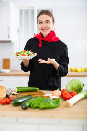 Smiling female chef in black uniform offering plate of vegetable saladの写真素材