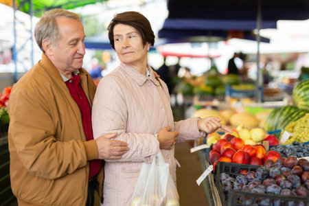 Aged man and woman customers buying peaches in open-air marketの写真素材